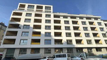 Moderne Wohnhausfassade mit vielen Balkonen und großen Fenstern unter blauem Himmel.