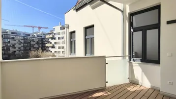 Heller Balkon mit Holzboden und Glasgeländer, bietet einen Blick auf die umliegenden Gebäude.