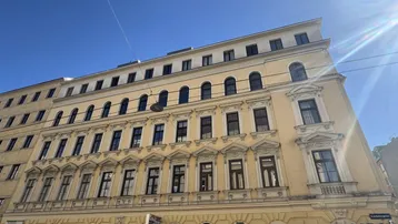 Historisches Gebäude mit gelber Fassade und vielen Fenstern unter strahlend blauem Himmel.