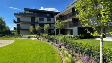 Moderne Wohnanlage mit gepflegtem Rasen, Bäumen und blühenden Pflanzen unter blauem Himmel.