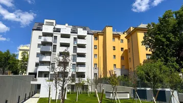 Modernes Wohngebäude mit weißen Fassaden und Balkonen, umgeben von einer grünen Außenanlage unter blauem Himmel.