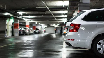 Dunkle Tiefgarage mit nassen Betonböden und parkenden Autos, beleuchtet von künstlichem Licht.