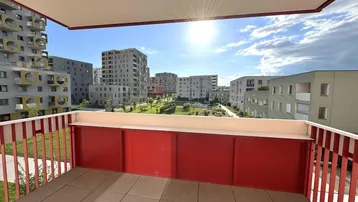 Heller Balkon mit rotem Geländer und weitem Blick auf moderne Wohngebäude und Grünflächen.
