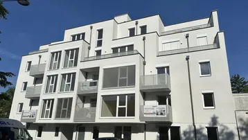 Moderne Wohnanlage mit mehreren Balkonen und großen Fenstern unter blauem Himmel.