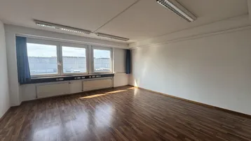 Geräumiges Büro mit großen Fenstern, Holzboden und Deckenbeleuchtung, ideal für Arbeitsbereiche.