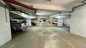 Geräumige Tiefgarage mit mehreren Stellplätzen und sichtbaren Versorgungsleitungen an der Decke.