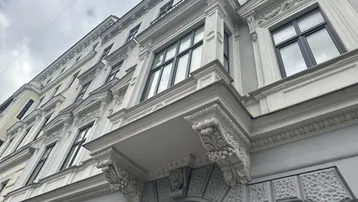 Detailaufnahme einer historischen Fassade mit reich verzierten Balkonen und Fenstern unter bewölktem Himmel.