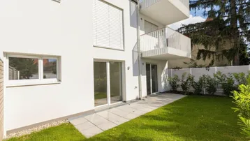 Moderner Neubau mit gepflegtem Rasen und Zugang zu einer kleinen Terrasse im Erdgeschoss.