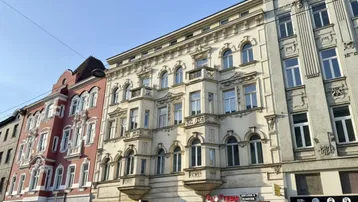 Historisches Mehrfamilienhaus mit reich verzierten Fassaden und Geschäften im Erdgeschoss an einer belebten Straße.