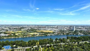 Weitläufige Luftaufnahme der Stadt mit Fluss, Grünflächen und Wohngebäuden unter blauem Himmel.