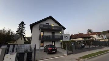 Modernes Mehrfamilienhaus mit Balkonen und gepflasterter Einfahrt bei Dämmerung.