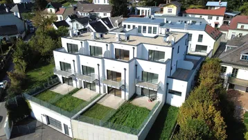 Modernes Wohngebäude mit Flachdach, Balkonen und privaten Gärten in einer grünen Umgebung.