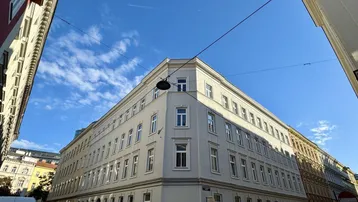 Eckgebäude mit klassischer Architektur und vielen Fenstern in städtischer Umgebung.