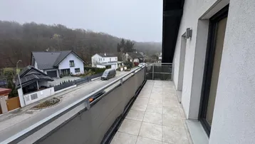 Geräumiger Balkon mit Fliesenboden und Blick auf die umliegende Wohngegend und Hügel.