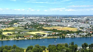 Luftaufnahme einer urbanen Flusslandschaft mit Stadtbebauung, grünen Ufern und weitem Blick in die Ferne.