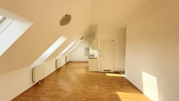 Heller Wohnbereich mit Dachschrägen, mehreren Dachfenstern und integrierter Küchenzeile.