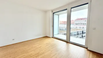 Helles, leeres Zimmer mit Parkettboden und Zugang zu einem Balkon, ideal als Wohn- oder Schlafzimmer.
