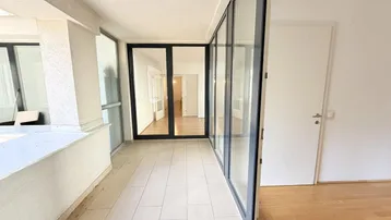 Helle Loggia mit Fliesenboden und großen Glasfronten, die den Blick nach innen freigeben.