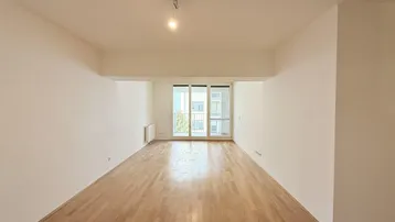 Helles, leeres Wohnzimmer mit Parkettboden und Zugang zu einem Balkon.