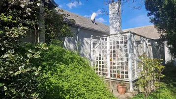 Seitlicher Blick auf das Haus mit üppiger Bepflanzung, einem Rankgitter und einem sonnigen Gartenbereich.