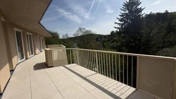 Geräumige, geflieste Terrasse mit weitem Blick ins Grüne und auf bewaldete Hügel.