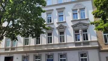 Historisches Mehrfamilienhaus mit klassischer Fassade, großen Fenstern und Bäumen im Vordergrund.