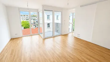 Helles Wohnzimmer mit Parkettboden, weißen Wänden und Zugang zu einem Balkon.