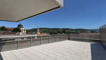 Große Dachterrasse mit hellen Fliesen und weitem Blick über die Landschaft und umliegende Gebäude.