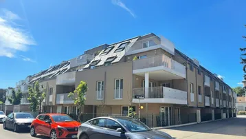 Modernes Mehrfamilienhaus mit mehreren Balkonen und Mansarddach in einer städtischen Umgebung.