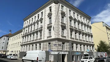 Elegantes Eckgebäude mit klassischer Architektur, vielen Fenstern und Geschäften im Erdgeschoss.