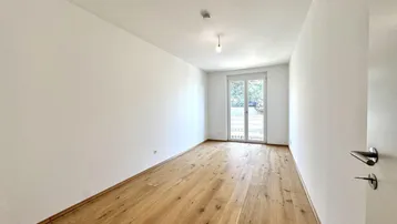 Helles Schlafzimmer mit Holzfußboden und einem französischen Balkon, der viel Tageslicht hereinlässt.
