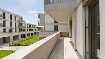 Geräumiger Balkon mit Fliesenboden und Blick auf die umliegenden Neubauten und Grünflächen.