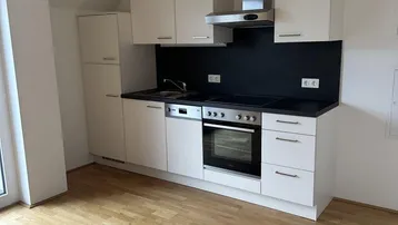 Moderne Einbauküche mit hellen Schränken, dunkler Arbeitsplatte und Holzboden in einem offenen Raum.