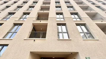 Blick von unten auf die moderne Fassade eines Mehrfamilienhauses mit zahlreichen Balkonen und Fenstern.