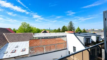 Panoramablick von einem Balkon über die Dächer der Stadt und grüne Umgebung unter blauem Himmel.