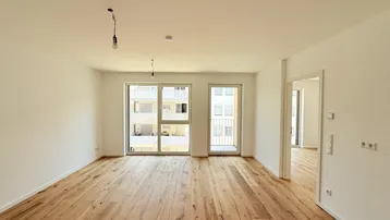 Helles, leeres Wohnzimmer mit neuem Holzboden und großen Fenstern, die viel Tageslicht hereinlassen.