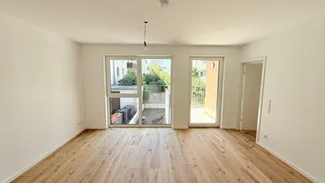 Helles, leeres Zimmer mit Holzboden und Zugang zu einem Außenbereich, bereit zur Einrichtung.