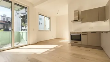 Helles, offenes Wohnzimmer mit integrierter Küche, Holzboden und Zugang zum Balkon.