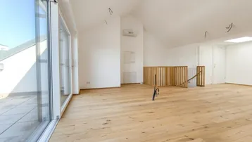 Geräumiger, heller Wohnbereich mit Holzboden, Dachschrägen und Zugang zu einer Terrasse.