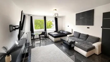 Moderner Wohn- und Schlafbereich mit dunklen Fliesen, bequemer Couch und großem Fenster.