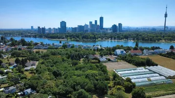 Luftaufnahme der Stadt Wien mit Donau, Wohngebieten, Grünflächen und der Skyline im Hintergrund.