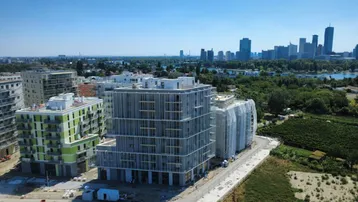 Luftaufnahme von modernen Wohngebäuden im Bau mit Stadtpanorama und Fluss im Hintergrund.
