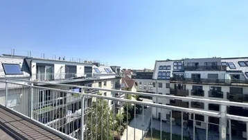 Blick von einem modernen Balkon mit Holzbelag auf umliegende Gebäude und den blauen Himmel.