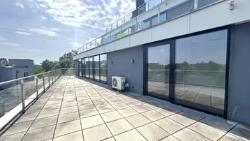 Große Dachterrasse mit Fliesenboden und Glasgeländer, bietet einen weiten Blick über die Umgebung.