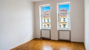 Helles Zimmer mit Fischgrätparkettboden und Blick auf die gegenüberliegenden Gebäude.