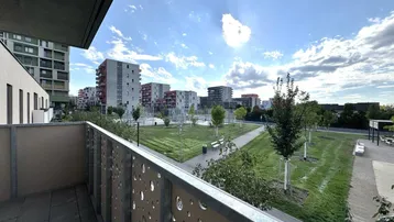 Balkon mit Blick auf eine moderne Wohnsiedlung und grüne Parkanlagen unter blauem Himmel.