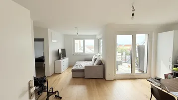 Helles Wohnzimmer mit Holzboden, Sofa und Zugang zu einem Außenbereich mit Stadtblick.