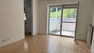 Heller Raum mit Parkettboden, weißen Wänden und Zugang zu einem Balkon mit Bergblick.
