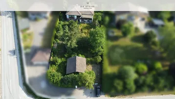 Luftaufnahme eines Grundstücks mit Wohnhaus, Nebengebäude und viel Grünfläche an einer Straße.