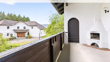 Balkon mit Außenkamin und Blick auf das umliegende Grundstück mit viel Grün.